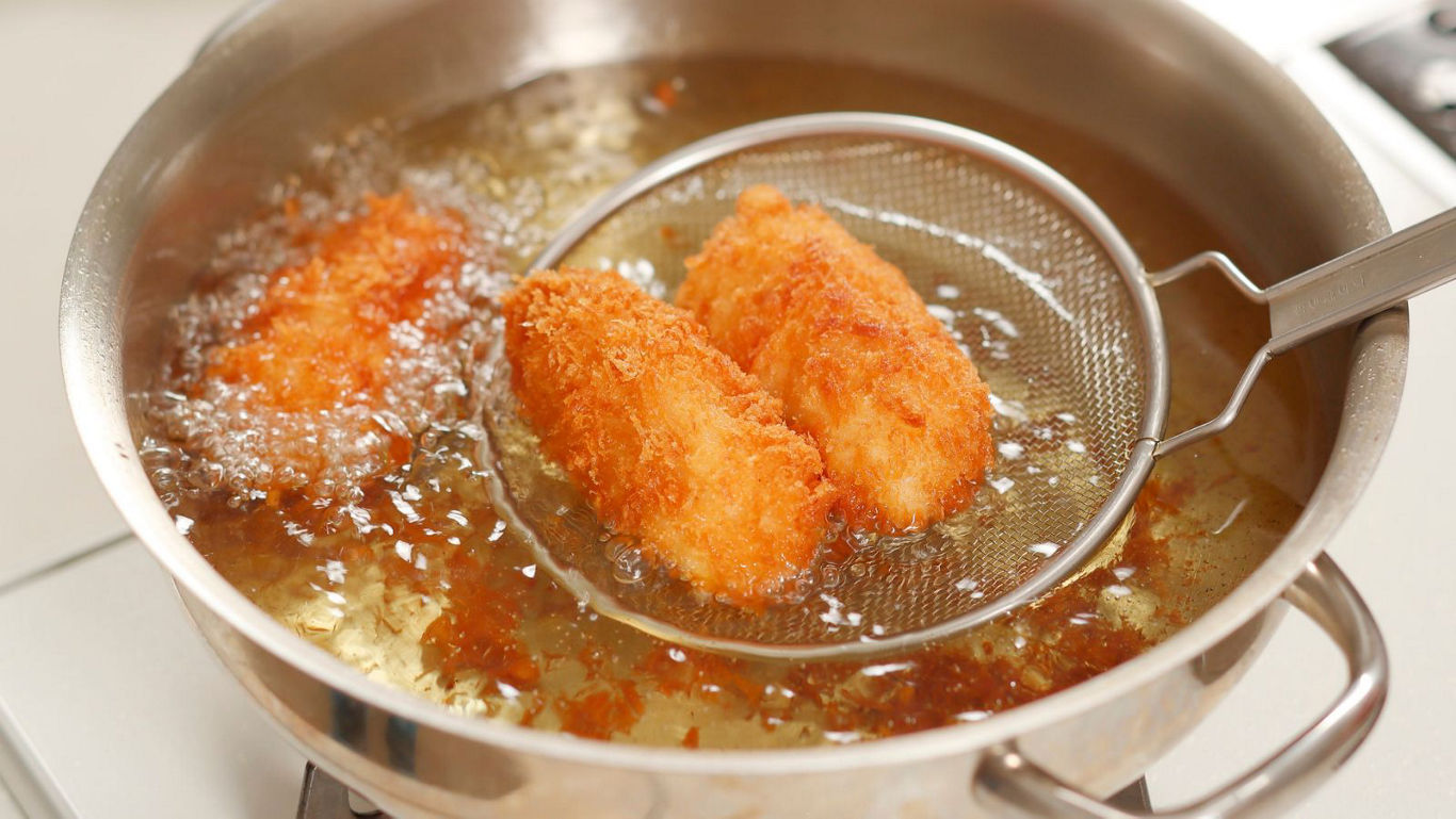 Golden breaded croquettes deep frying in pan