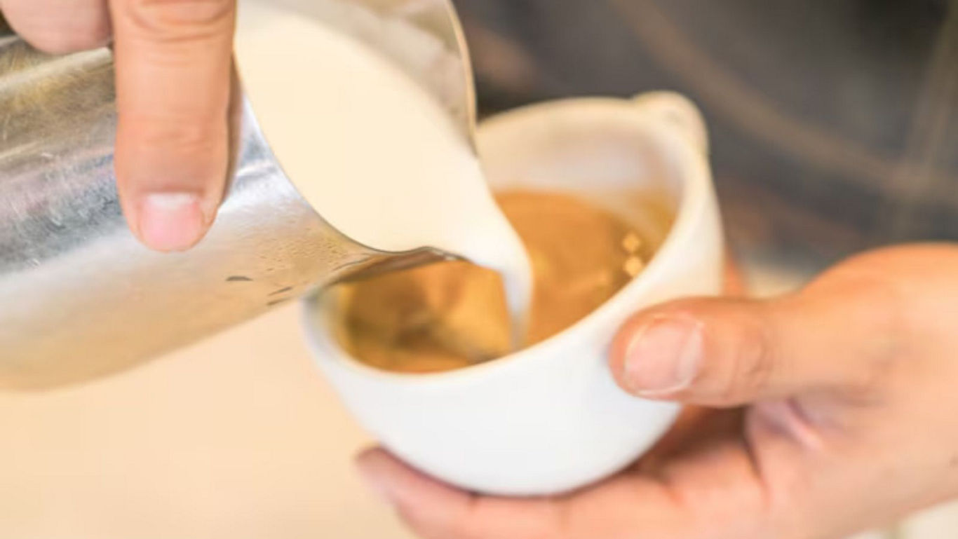 Barista pouring milk into hot coffee