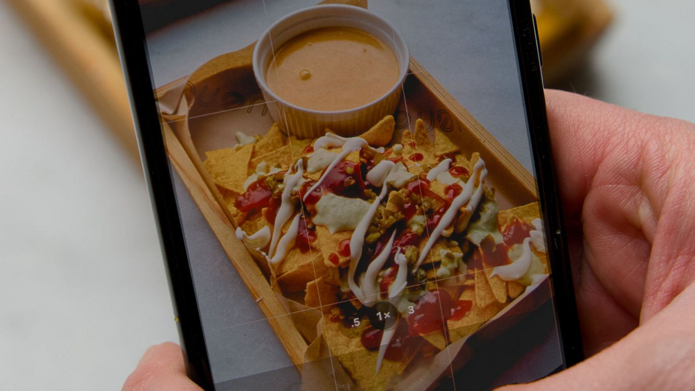 Person photographing loaded nachos on smartphone