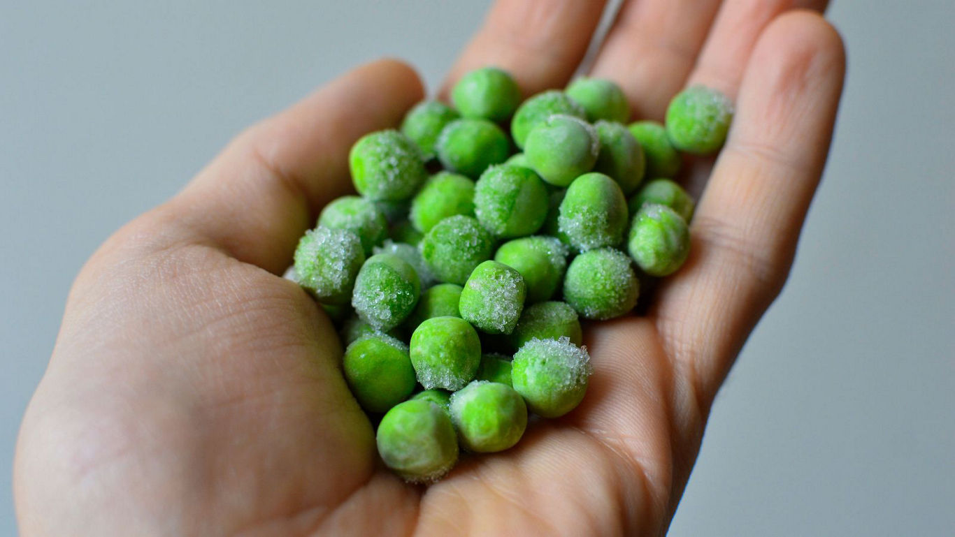 Hand holding frozen green peas close-up