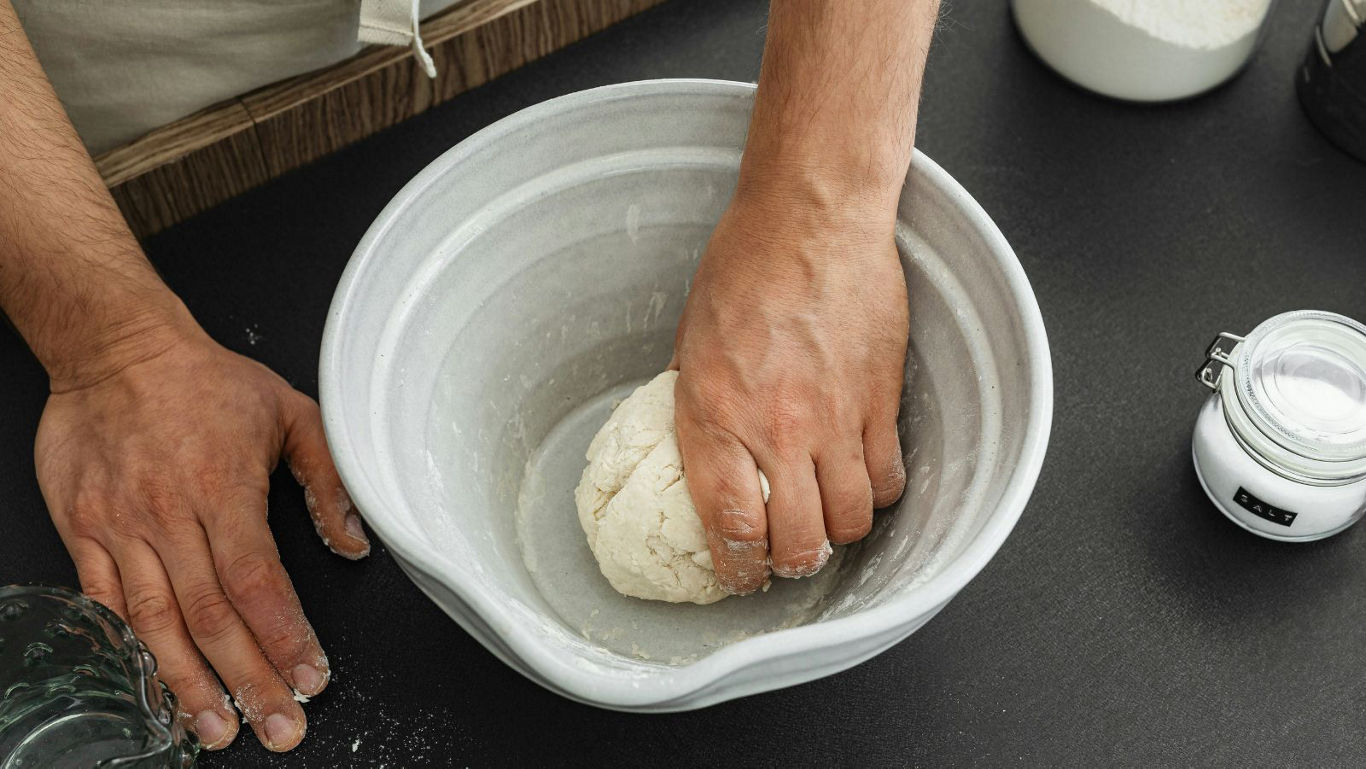 Person kneading dough in a ceramic mixing bowl