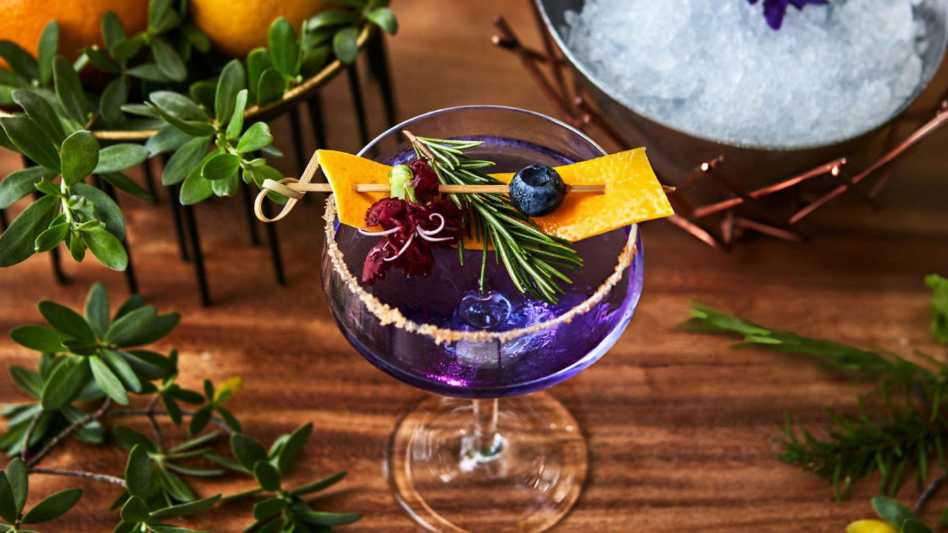 Vibrant purple cocktail with citrus and herb garnish
