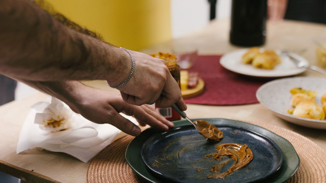 Person spreading peanut butter on dark plate