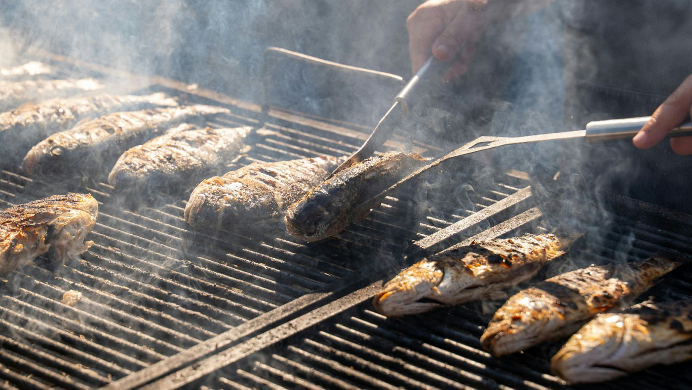 Whole fish grilling over smoky outdoor barbecue