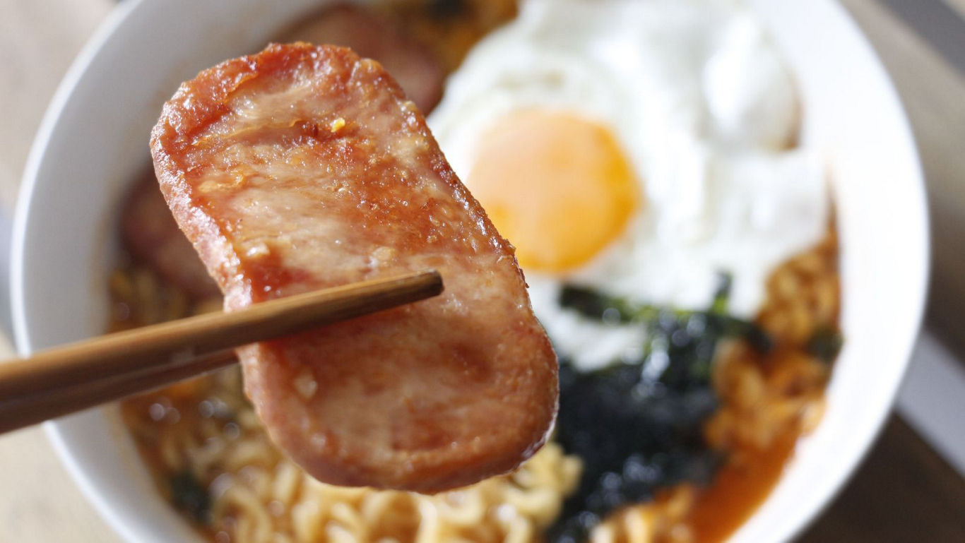 Chopsticks holding spam over ramen bowl