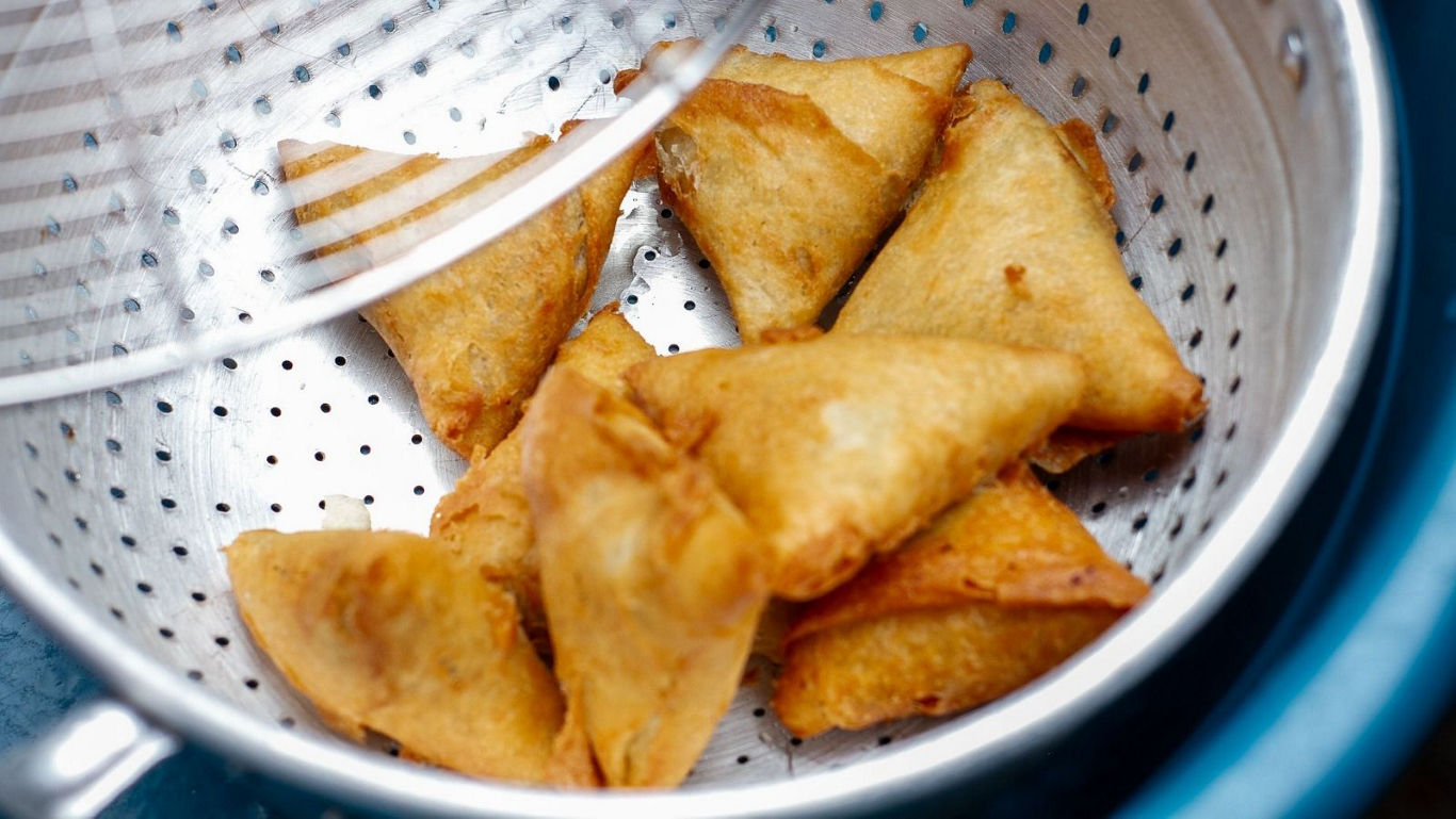 Freshly fried samosas in metal strainer