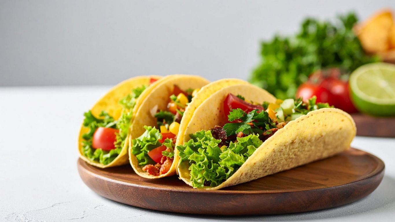 Three fresh vegetable tacos on wooden plate