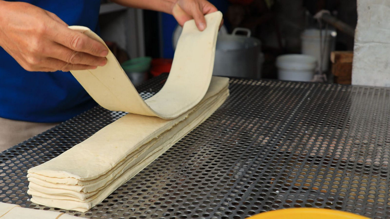 Worker folding layered dough sheets on table