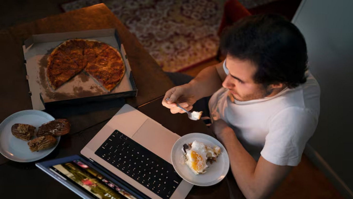 Person eating pizza and dessert while watching laptop