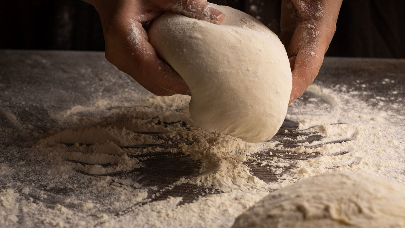 Hands kneading dough on floured surface