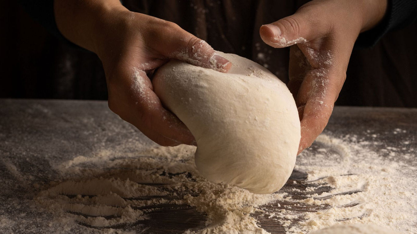 Hands Kneading Dough on Floured Surface