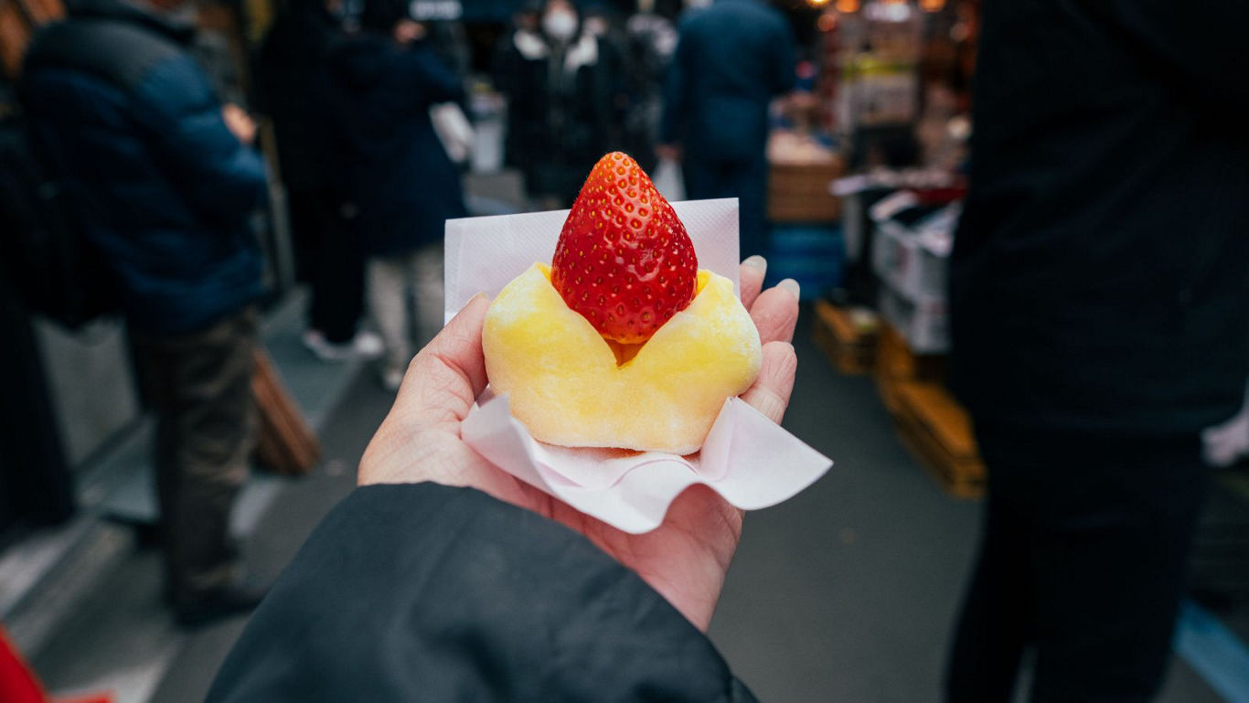 Hand holding strawberry dessert in street market