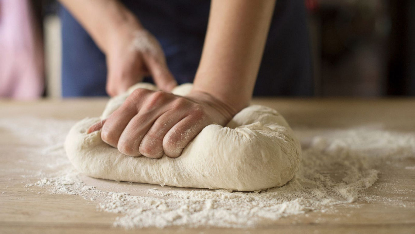 Baker kneading fresh dough on floured table