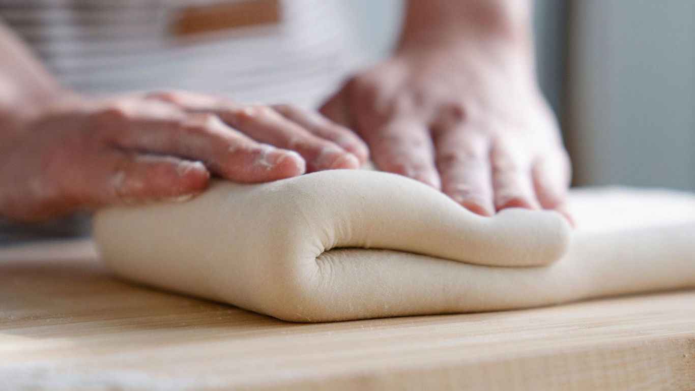 Hands folding fresh dough on wooden table