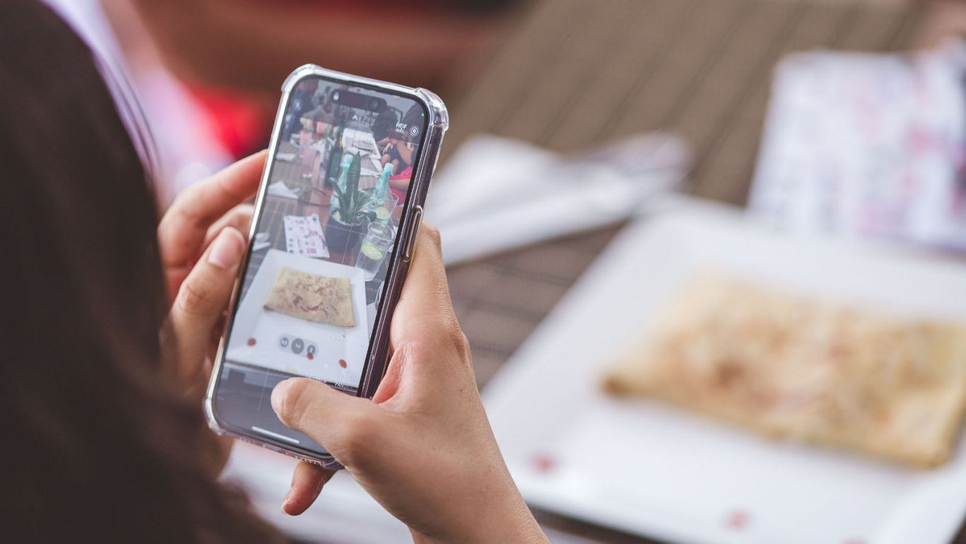 Person photographing food with smartphone outdoors
