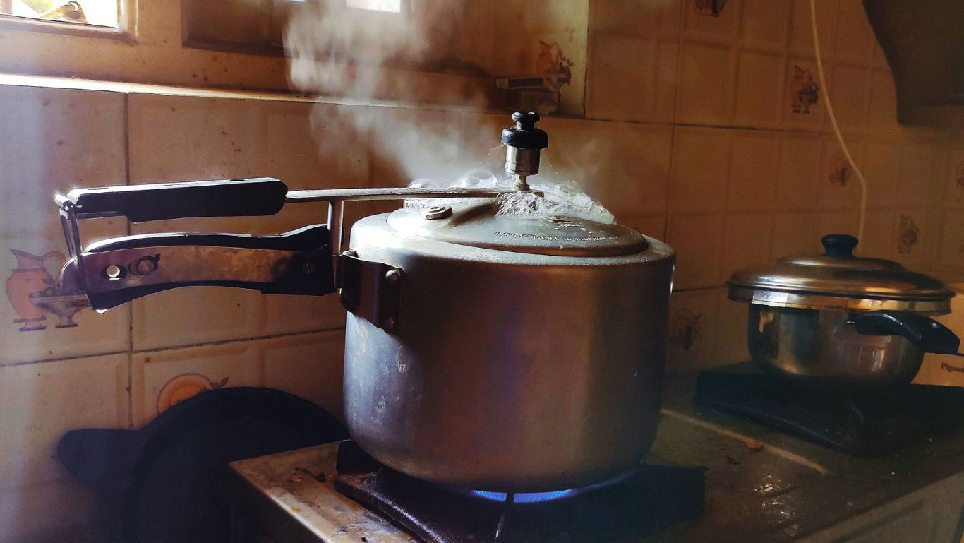 Pressure cooker releasing steam on kitchen stove