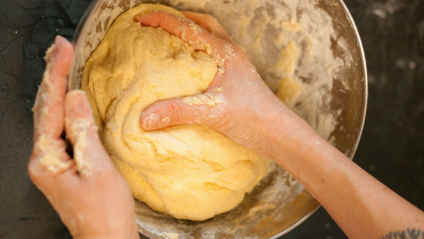 Hands kneading soft dough in metal bowl