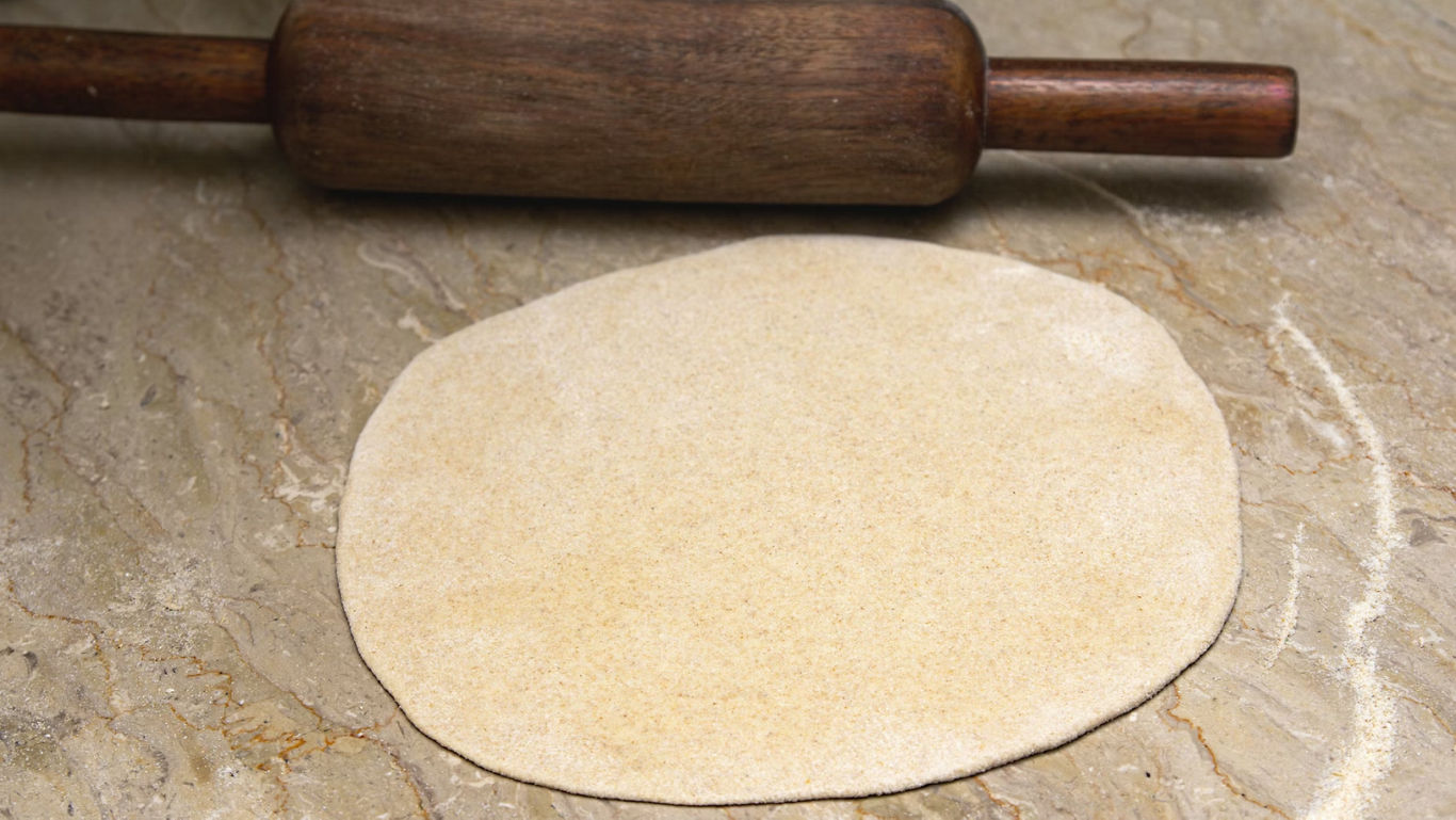 Rolled dough with wooden rolling pin on countertop