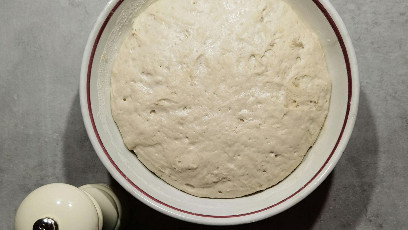Risen bread dough in ceramic mixing bowl
