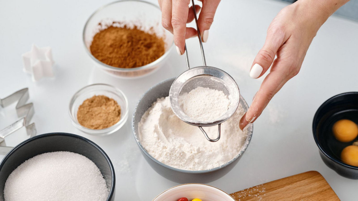 Home baker sifting flour for dessert preparation