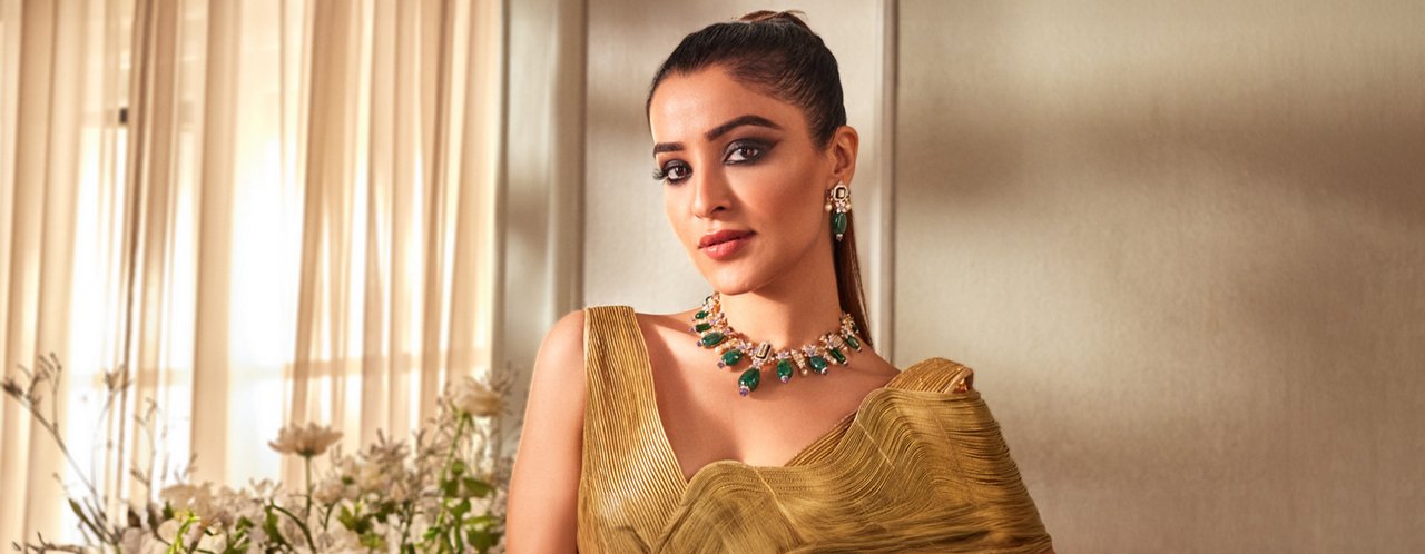 Opulent green gemstone necklace and matching earrings on a woman in a golden draped dress