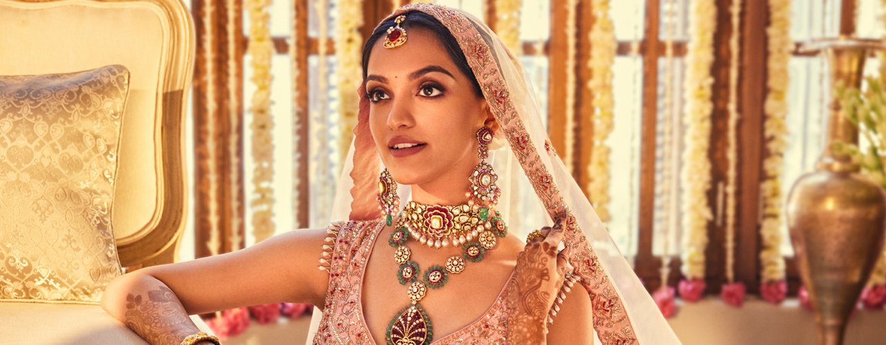 Bride in pink lehenga adorned with intricate multicolored gemstone necklace and matching earrings