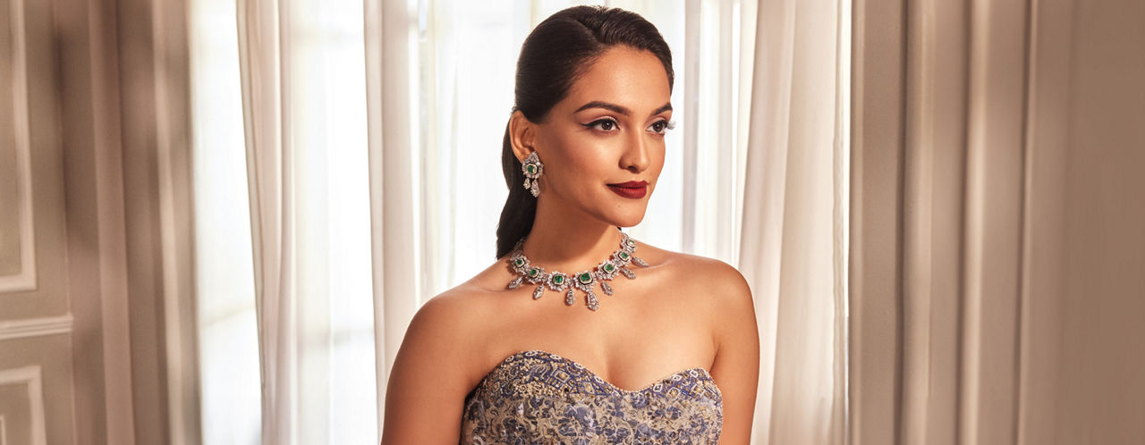 Elegant necklace and earrings set with emerald and diamond accents on a woman in a lavender gown