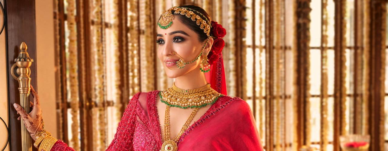 Indian bride showcasing elaborate gold and green gemstone necklace, earrings, and maang tikka.