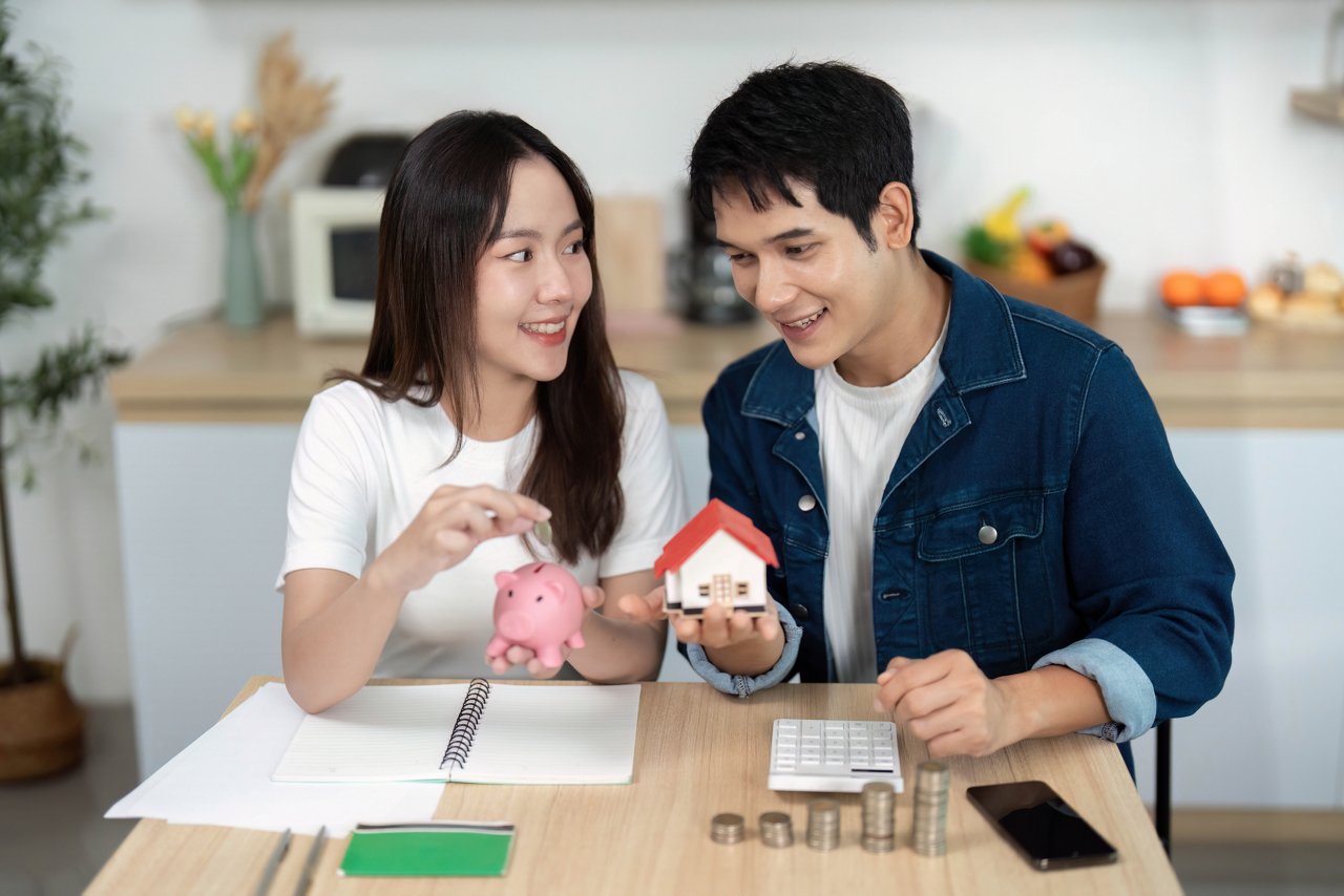 A couple engages in financial planning, using a piggy bank and notes to discuss savings strategies in a cozy kitchen setting.