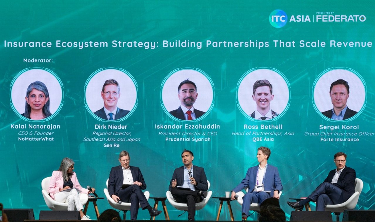 A business conference panel discusses insurance ecosystem strategy on a stage with a teal backdrop. Five speakers sit in chairs while a moderator on the left engages them in conversation. Above them, circular portraits display the names and titles of Kalai Natarajan, Dirk Nieder, Iskandar Ezzahuddin, Ross Bethell, and Sergei Korol. Event branding for ITC Asia and Federato appears at the top of the background along with the session title, “Insurance Ecosystem Strategy: Building Partnerships That Scale Revenue.” The setting is professional, with formal attire and a large audience-focused presentation environment.