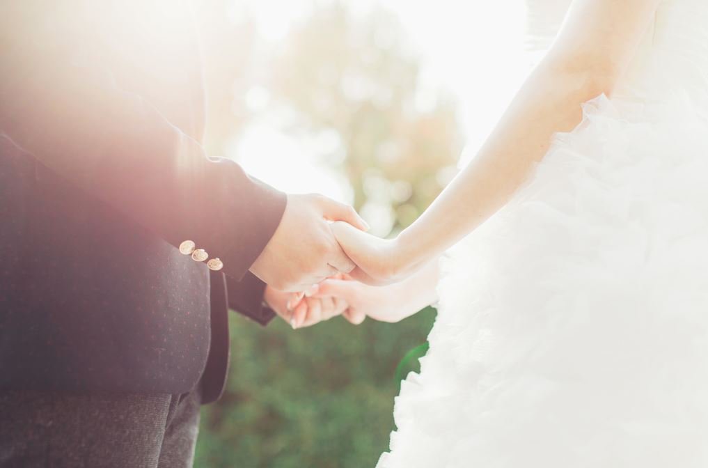 A close up of a bride and groom holding hands