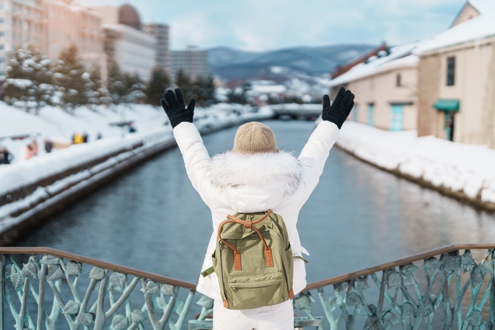 Woman tourist Visiting in Otaru, happy Traveler in Sweater sightseeing Otaru canal with Snow in winter season. landmark and popular for attractions in Hokkaido, Japan. Travel and Vacation concept