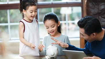 two daughters putting money into their piggy with father