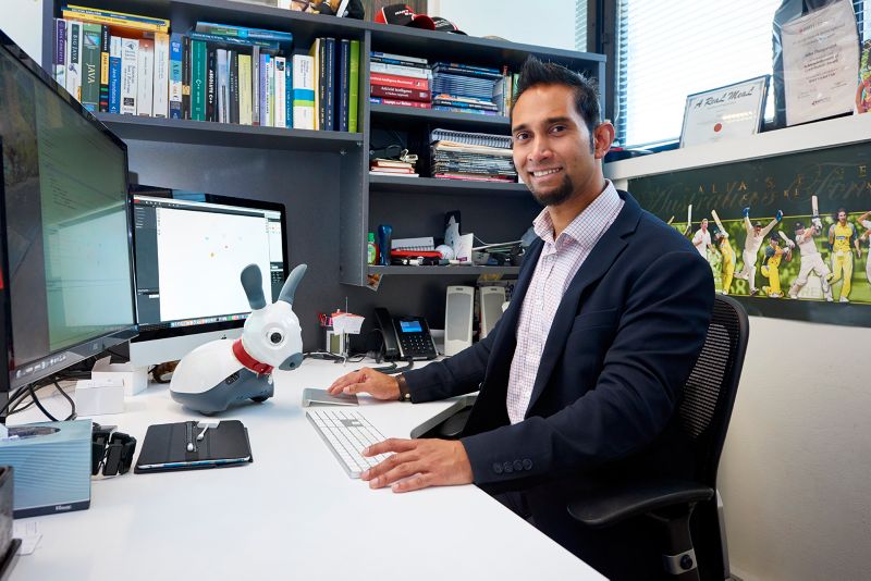 John Thangarajah sitting at his desk with his robot dog