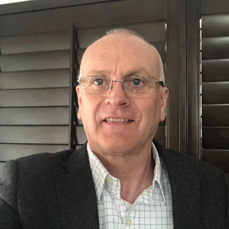 Profile photo of Distinguished Professor Andy Ball. Andy is standing in front of a set of closed black window blinders. Andy is facing the camera and staring just to the left of it, wearing a buttoned up shirt and blazer.