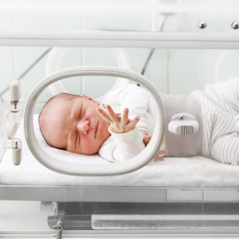 A newborn baby in an incubator in a hospital ward.