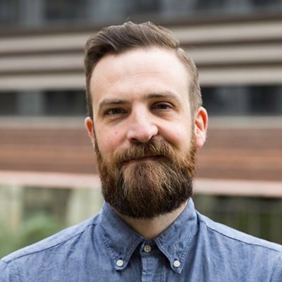 Profile photo of Ben Cooke smiling towards the camera against an out of focus background of a building and trees