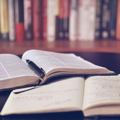 Books open in front of bookshelf. Square photo.