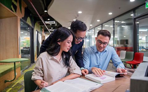 two students and a male lecturer engaged in reading a book 