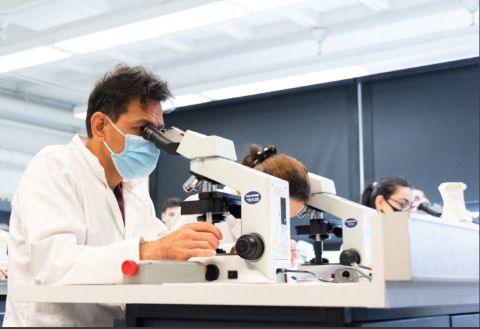 Text on left reads How RMIT has transformed STEM for 2023 and beyond. On right a photograph of three people in white lab coats sit at microscopes.