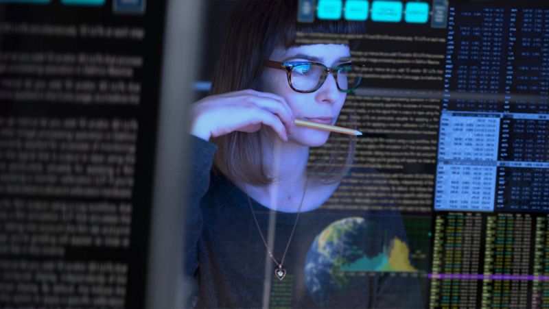 Stock image of a young woman studying a see through computer screen & contemplating.