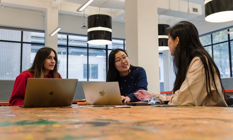 Three students working on computers and talking.