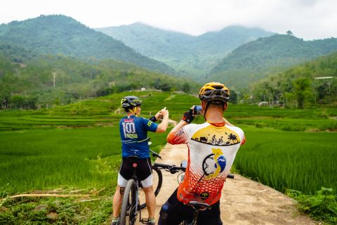 two cyclists taking pictures while stopping between some paddy fields