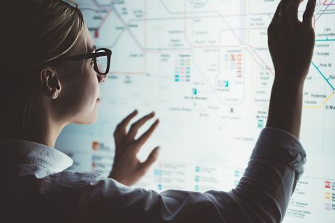 Digital monitor with public transport subway map. Female standing at big display with advanced innovative technology. Young woman touching with finger sensitive screen while selecting surface option