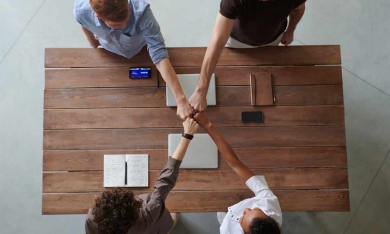 Four people sitting at a table fist bumping 