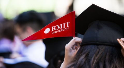 Close up of a student wearing a graduation cap and holding a red RMIT flag.