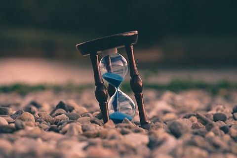 Hourglass with blue sand inside. On top of rocks.