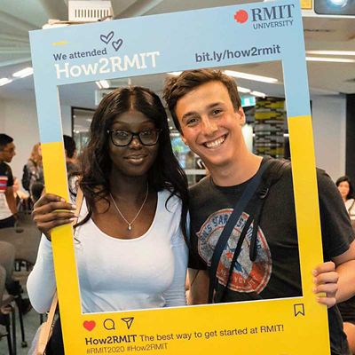 Two students stand with a mock-Instagram cardboard cut-out that advertises How2RMIT.