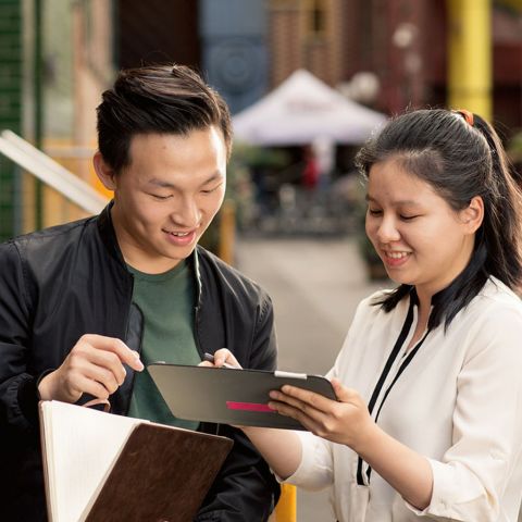 Two international students are looking at a tablet together, with the female student holding the device.