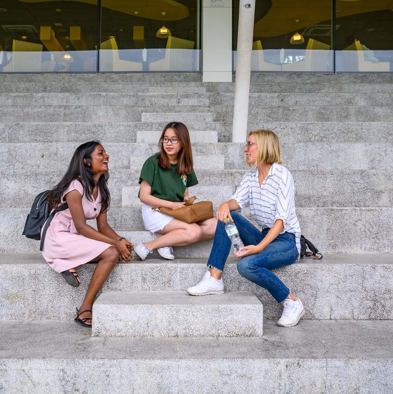 3 international students - Vietnamese, Danish and Sri Lankan, sitting on bleachers having a chat